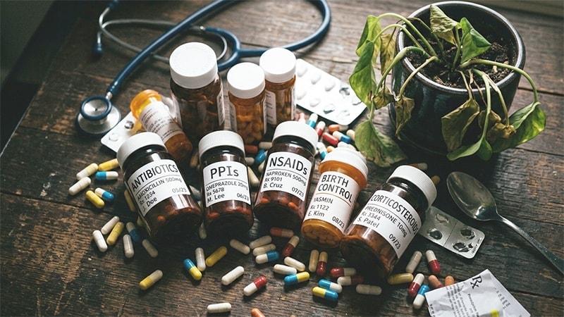 Flat lay of prescription medication bottles including antibiotics, PPIs, NSAIDs, birth control, and corticosteroids on a dark surface.